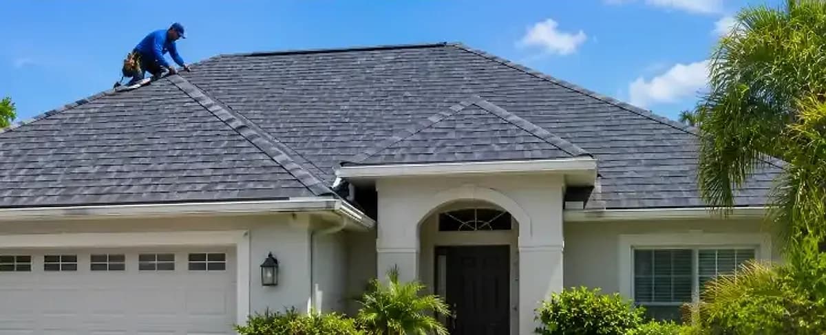 Roofer finishing a new dark architectural shingle roof on the same hip-roof home