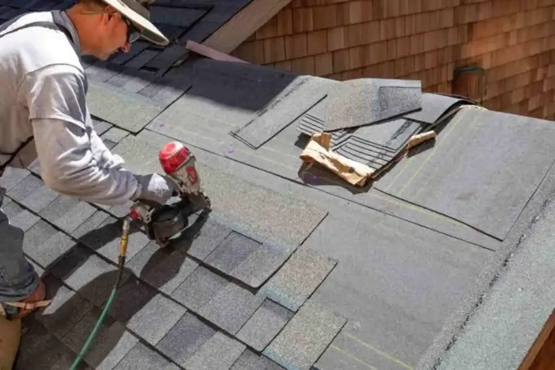 Roofer nailing replacement shingles into a damaged section of roof where it meets the wall