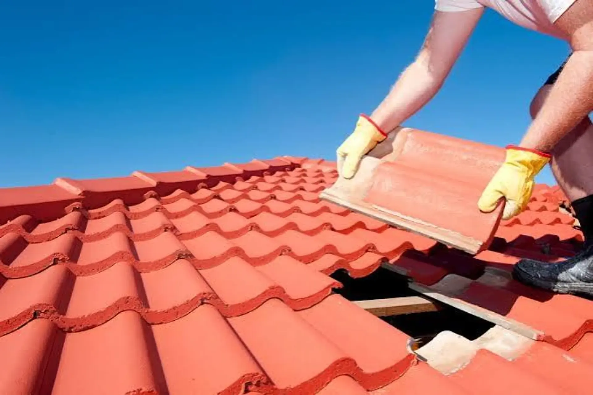 Roofer in work gloves lifting a red S-profile roof tile during a tile roof replacement