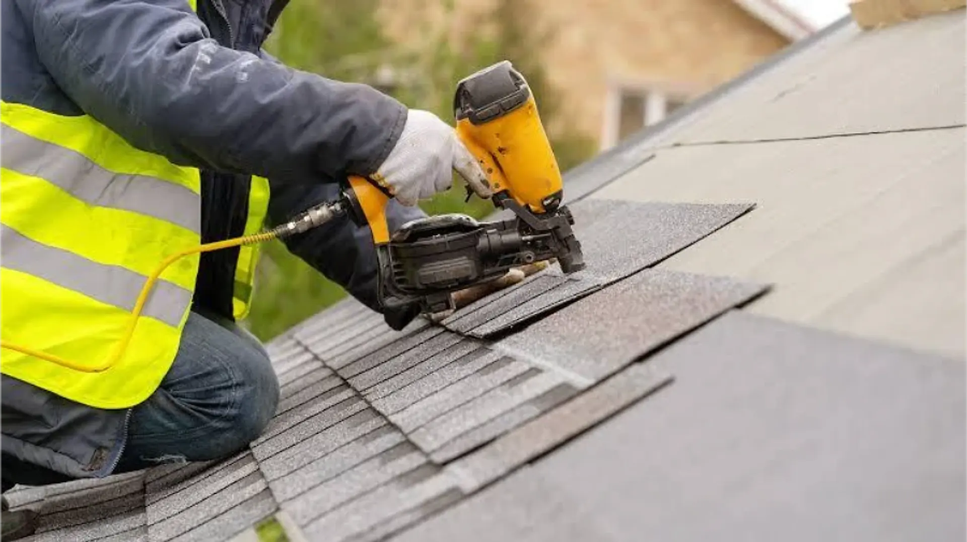 Roofer installing new asphalt shingles with a roofing nail gun during a roof replacement