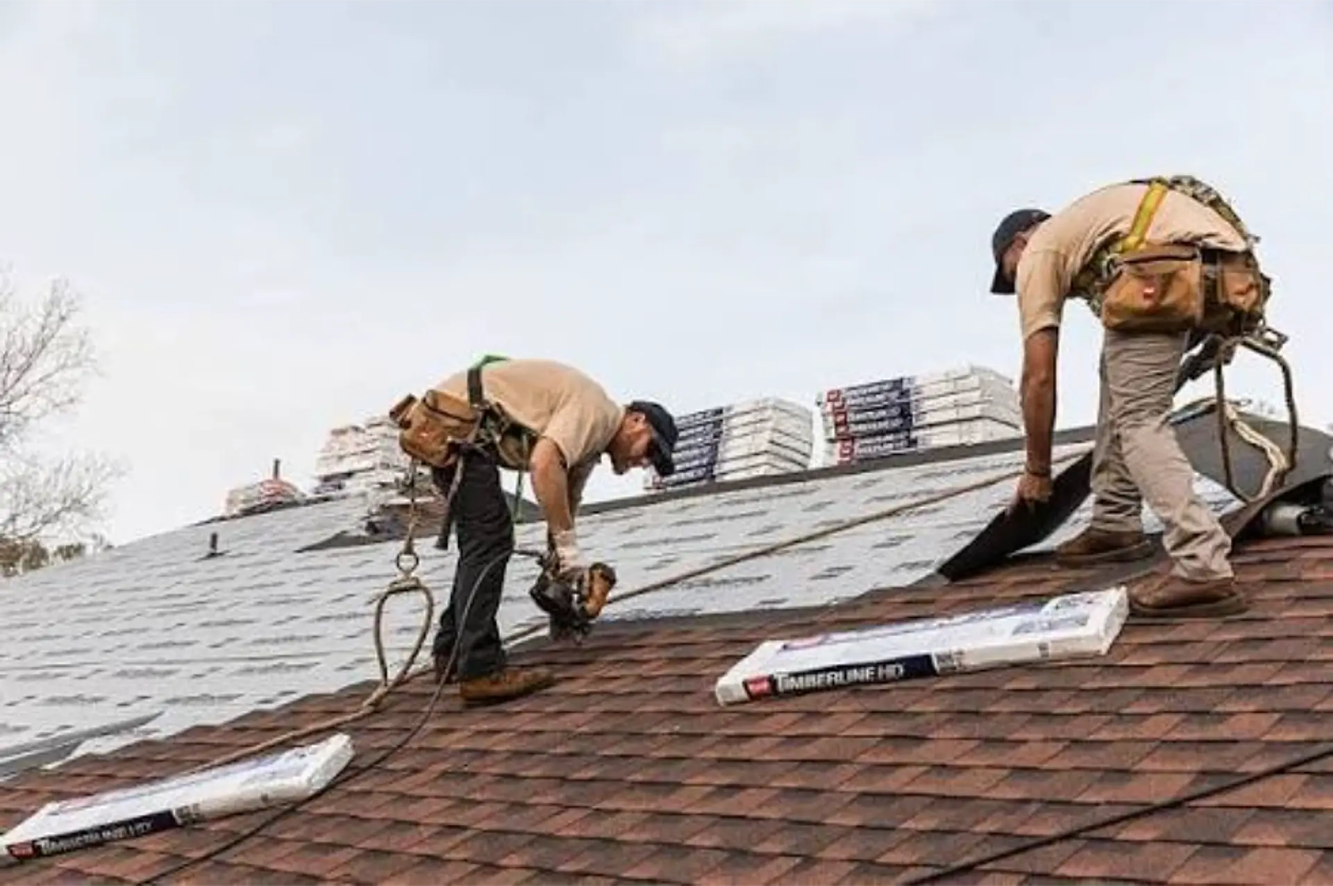 Two roofers installing new architectural shingles on a home, with shingle bundles staged on the roof