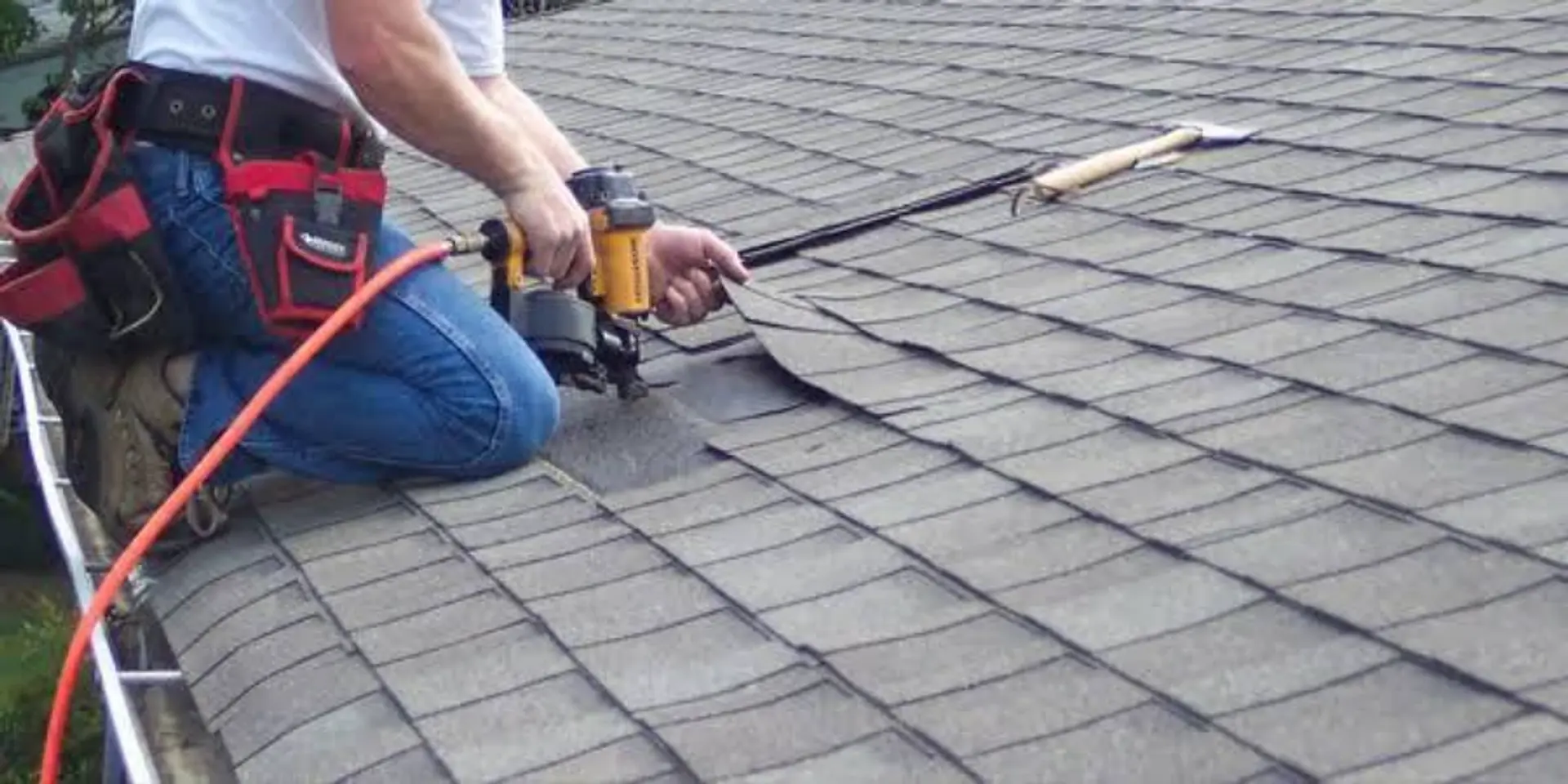 Roofer nailing new asphalt shingles near the roof edge during a shingle roof replacement